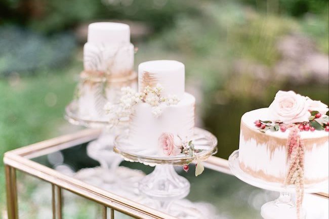 Several gold and white wedding cakes atop a mirrored table