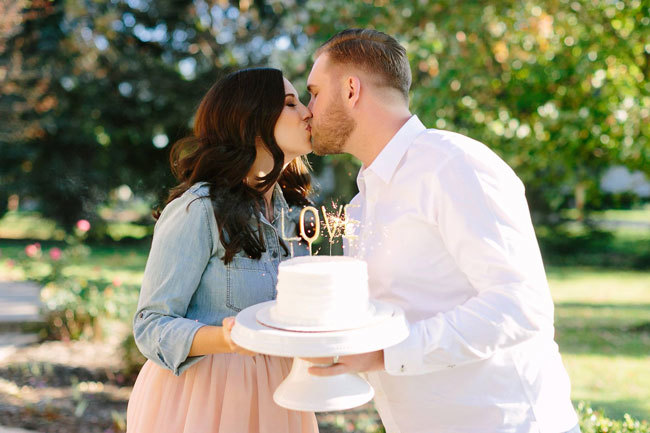 A newly-engaged couple kiss in front of a sparkling cake
