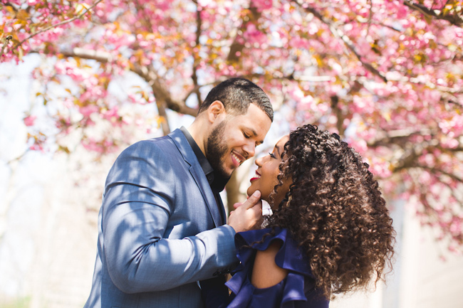 A couple takes engagement photos under cherry blossom trees
