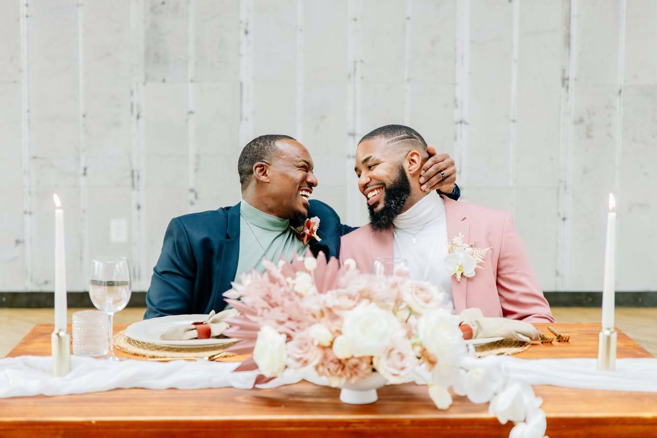 Two grooms in pink and blue suits smile at each other | Wedding Checklist by Here Comes The Guide